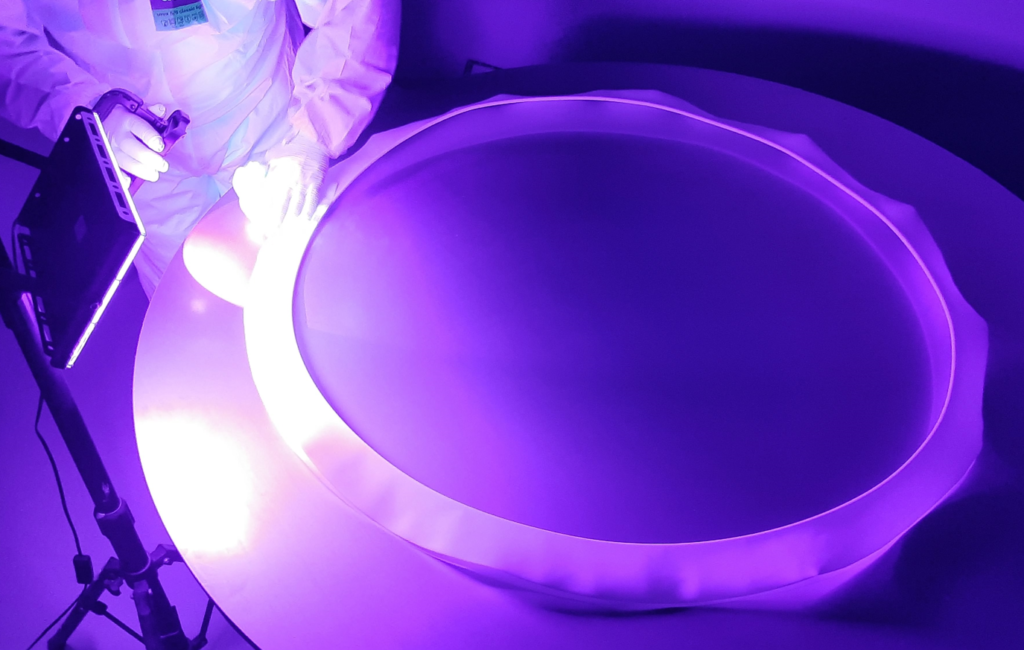 A person in protective gear examines a large round object under bright purple lighting.
