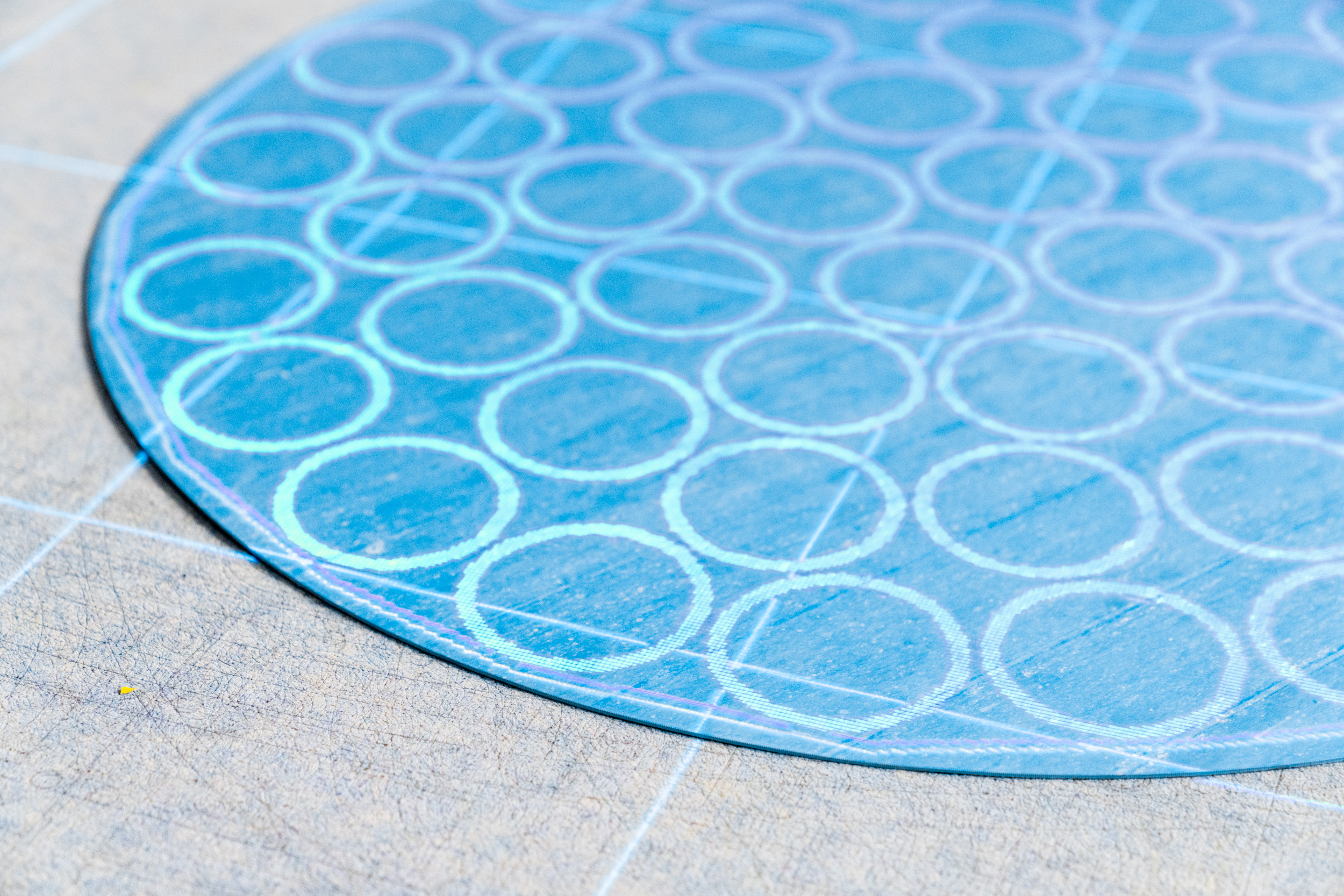 Close-up of a circular blue wafer with a grid of etched circles on a light-colored surface.