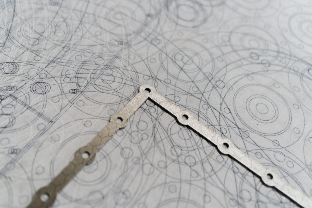 Close-up of a metal strip on paper with overlapping circular and straight pencil sketches.