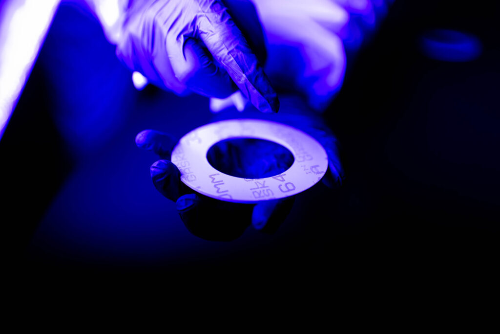 A gloved hand holds a circular object with markings, illuminated by blue and purple light.