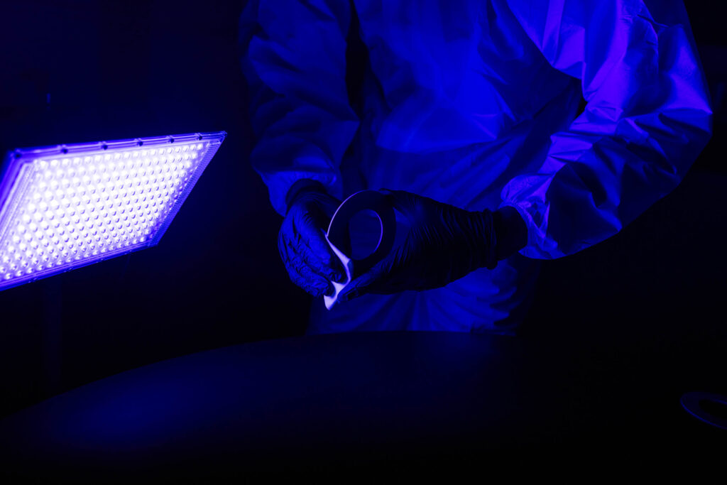 Person in gloves and protective suit handling material under blue light from a bright LED panel.